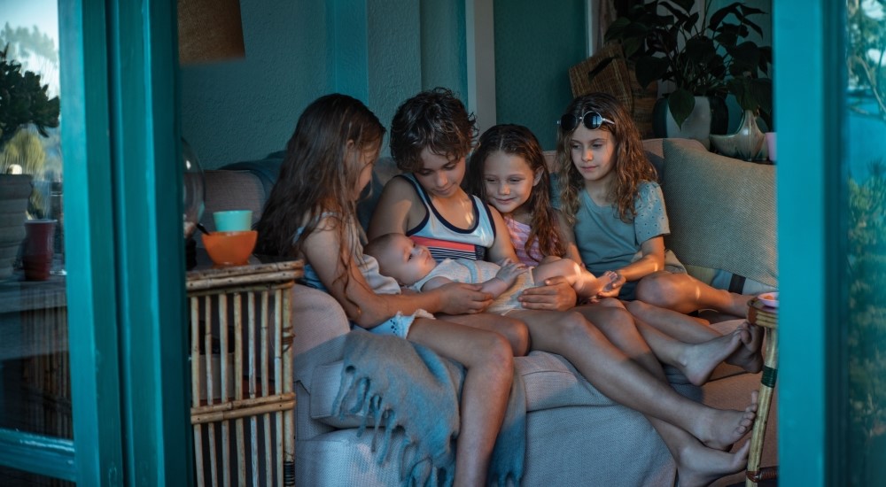 Group of children cradling baby on a sofa