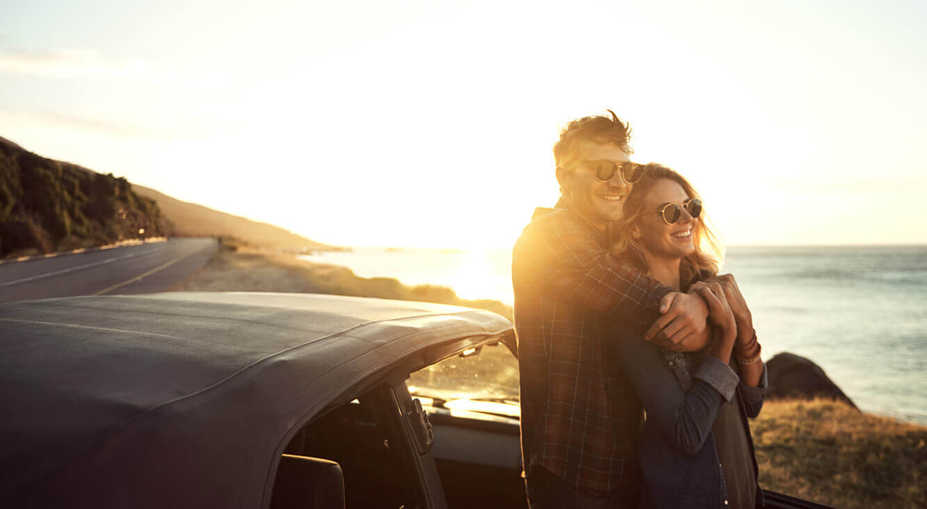 Third Party Car insurance - Young couple standing next to a car in dappled sunlight