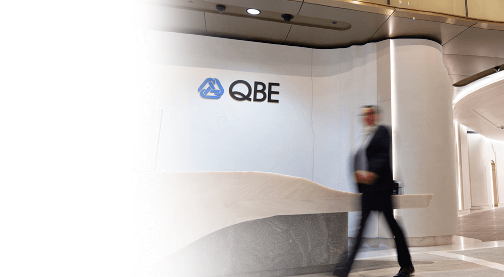 Blurred businessman walking past the QBE logo on a wall in an office reception area