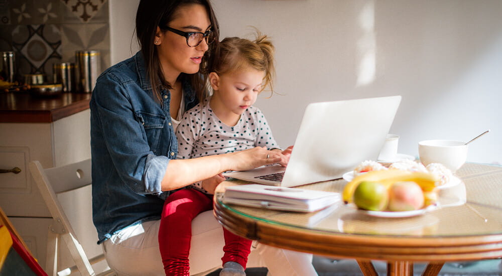 Mother with daughter sitting at table with laptop