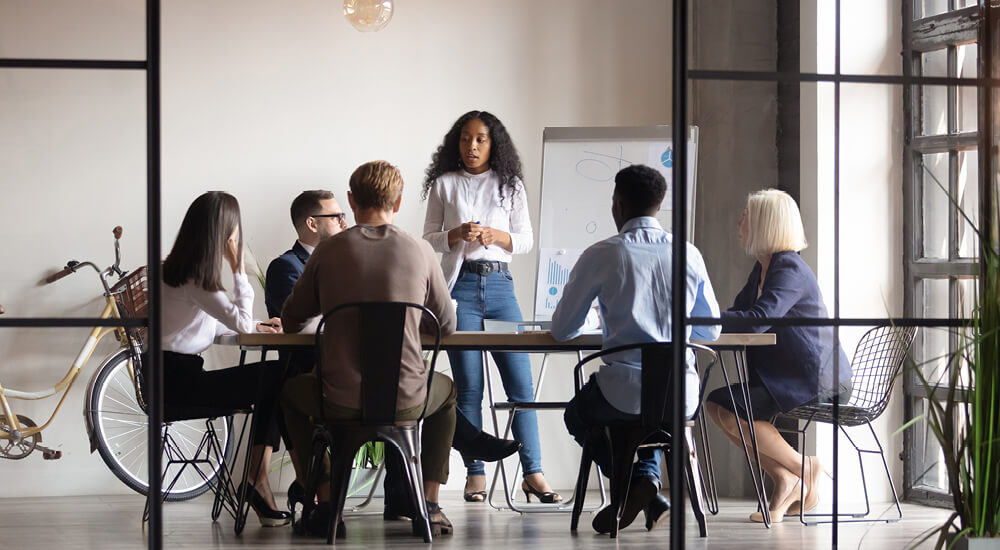 Looking through glass walled conference room at a woman presenting to her colleagues