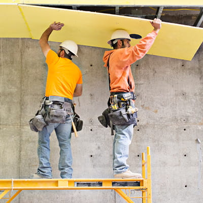 Two workmen installing plasterboard to a ceiling on a construction site