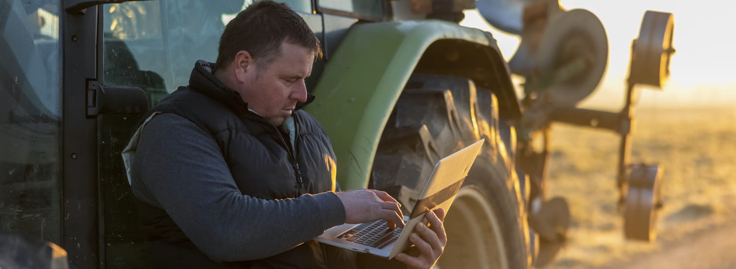 Farmer on his laptop while leaning against his tractor in a field