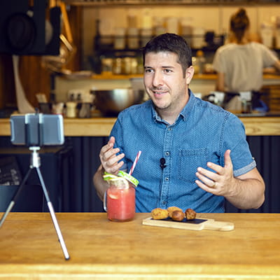 Middle-aged while man at a restaurant presenting to mobile phone propped on a tripod