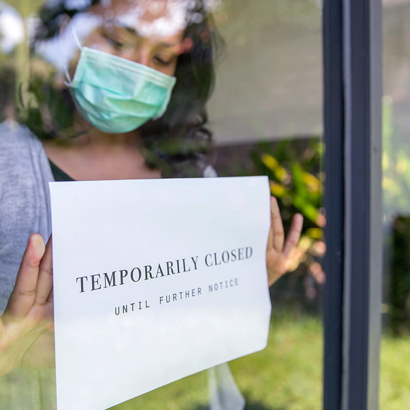 Woman wearing a face mask pinning a Temporary Closed sign to the door of her place of work