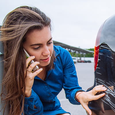 Woman on phone while looking at car damage