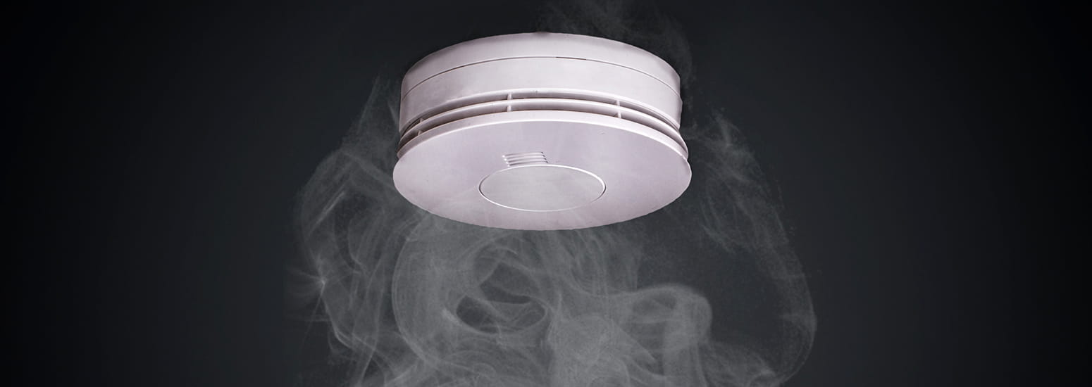 Close up of ceiling smoke alarm surrounded by smoke