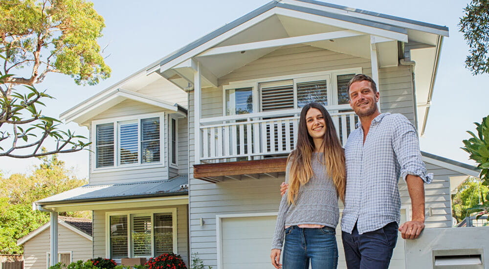 Home owners insurance - young home owners standing in the sunshine outside their 2-storey house