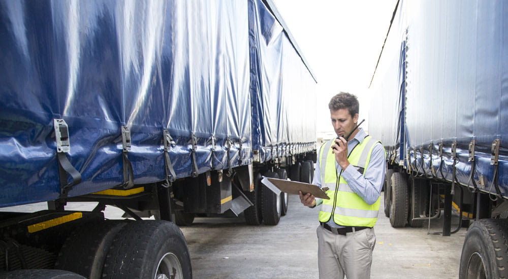 Carriers Load quote Info guide banner - Man talking into a radio standing between two trucks