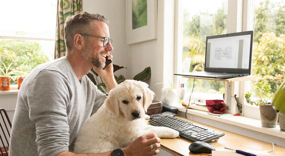 Man working from home with golden retriever puppy on his knee
