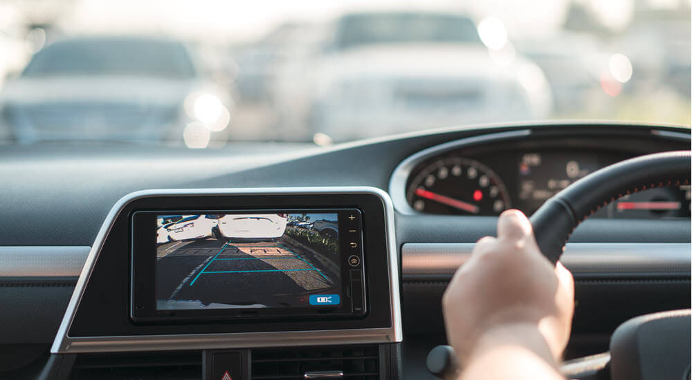 View from the car's back seat of the driver's hand on the steering wheel and a rear area video camera on the dashboard