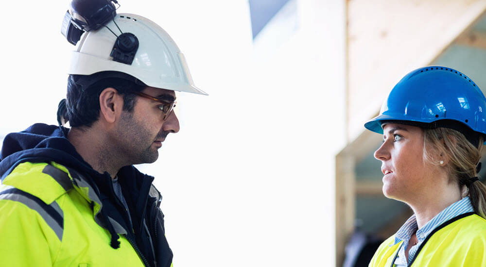 Male and female managers discussing over document at construction site