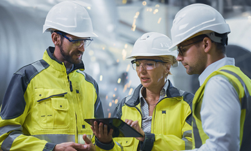 Two experts engineers in protective helmets and fluorescent vests dealing with construction site blueprints.