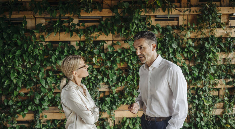Businessman and businesswoman talking in front of a wall of plants