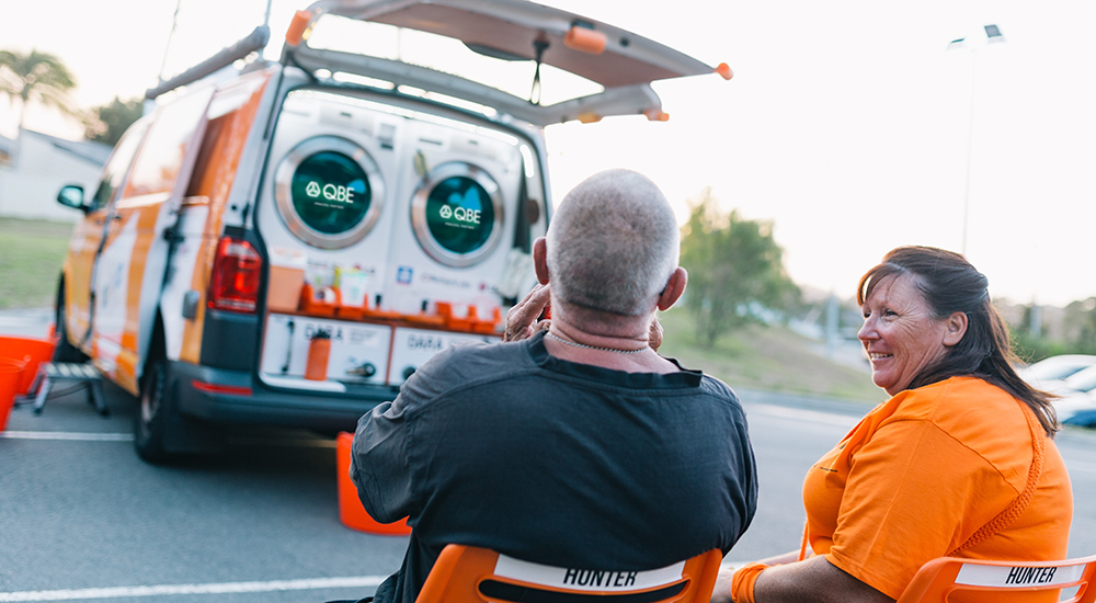 Volunteers sitting next to an Orange Sky van showing industrial washing machines