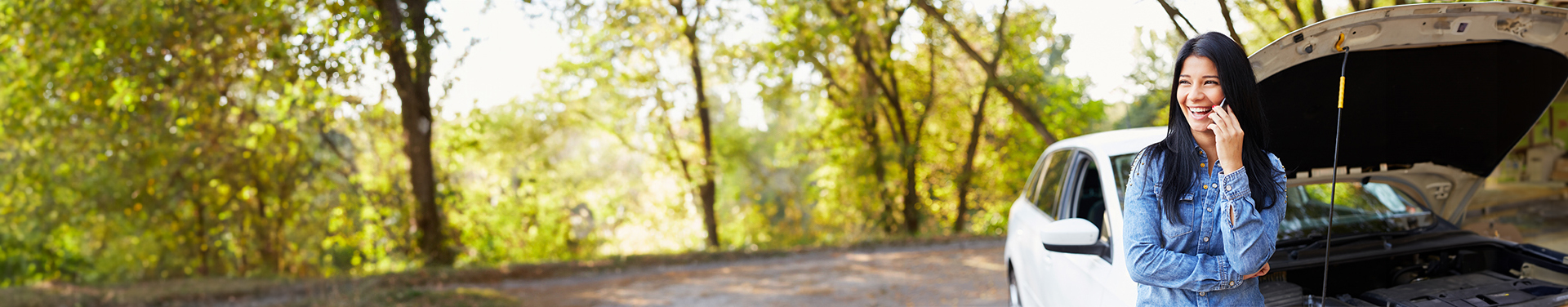 Woman talking on her mobile phone standing in front of her broken down car