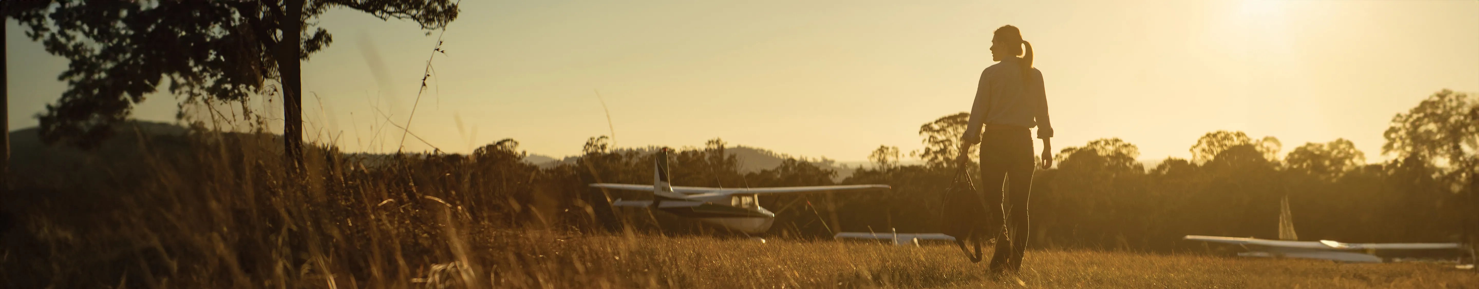 Rear view of female pilot walking towards light aircraft at dusk