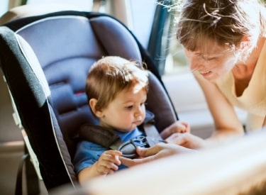 mother buckling seat belt for baby in car seat