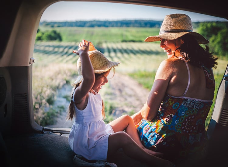 Car insurance - Woman and girl sititng in the boot of their vehicle overlooking the countryside