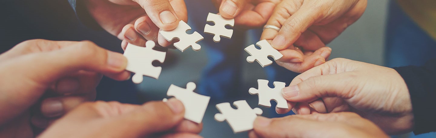 Jigsaw pieces being put together by group of hands