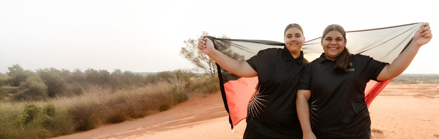 Two indigenous Australian girls holding up an Aboriginal flag near Alice Springs, Northern Territory