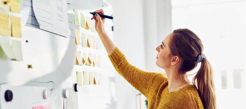 Consultant planning a business strategy on a whiteboard with sticky notes in a bright office, representing structured planning and professional risk management.