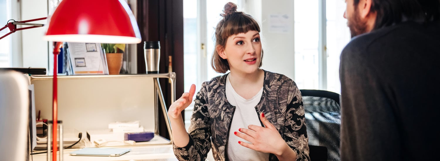 Woman sitting at desk talking to male colleague