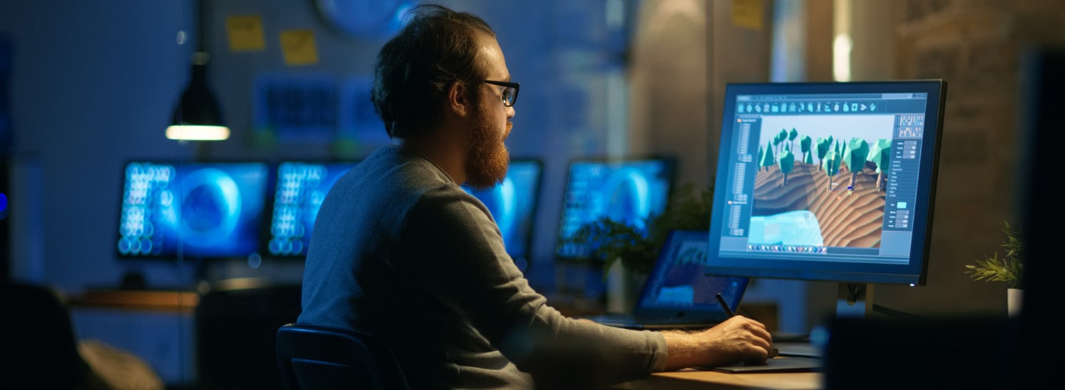 Rear view of man sitting in front of computer monitor at his work desk