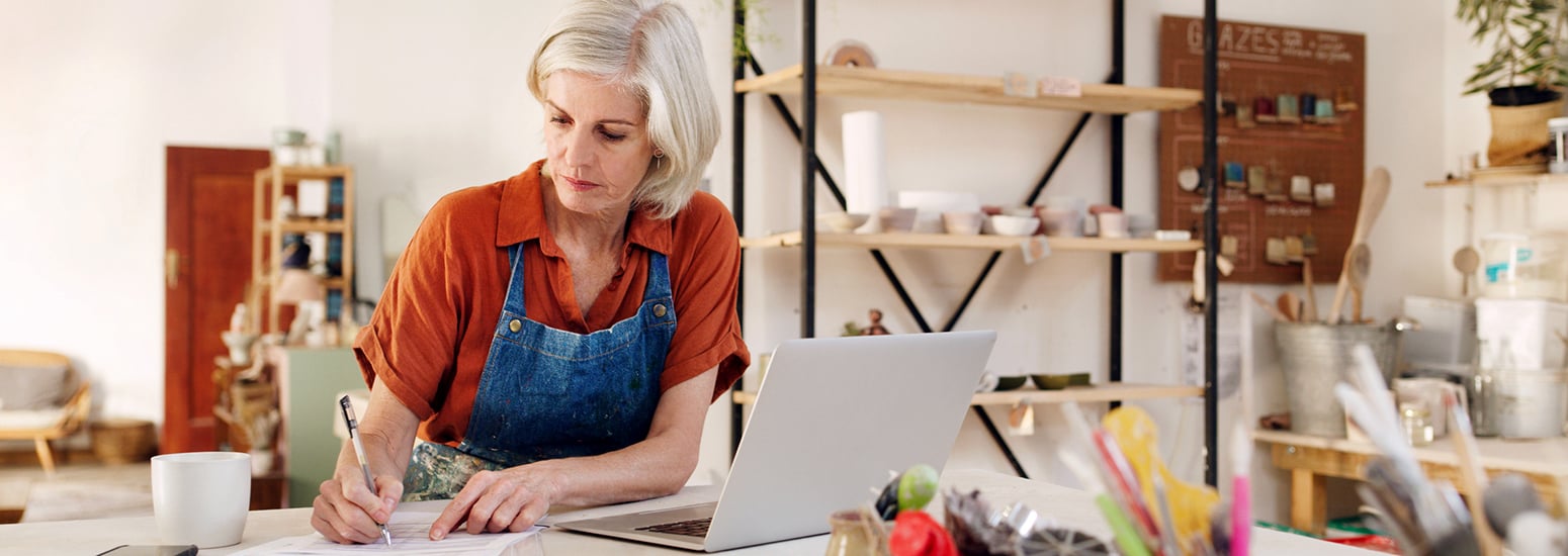 Female small business owner writing on paper with laptop open