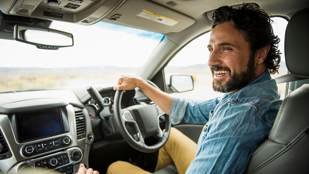Smiling man sitting in the driver's seat of his car with hand on the steering wheel