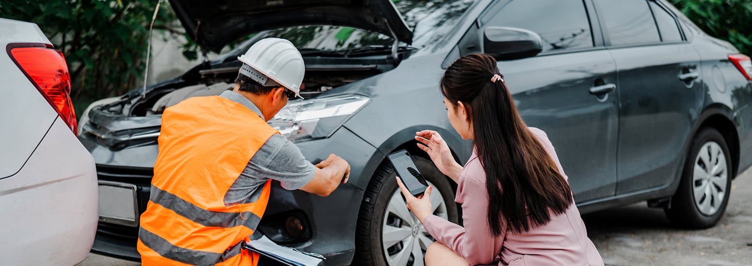 Man wearing hi-vis and woman holding phone examining front of car