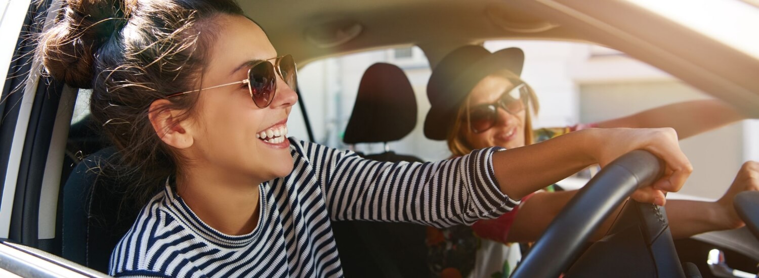 Portrait of two women sitting in car, wearing sunglasses, smiling.