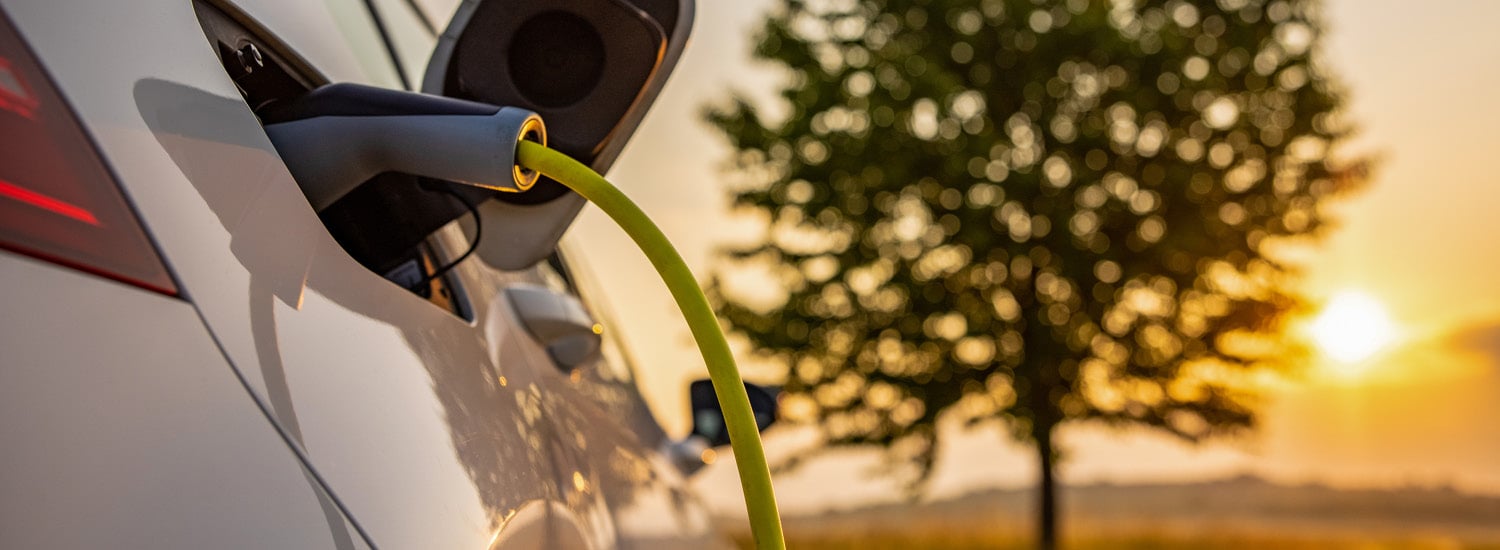 Close up of electric vehicle charging car with sun in background