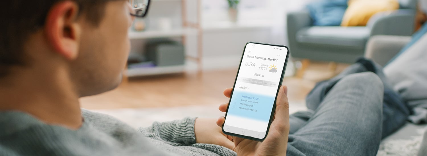 Man lounging on sofa looking at a weather app on his mobile phone