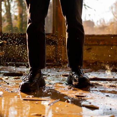 Close up of boots standing in water and mud after a storm has damaged a home