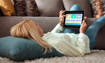 Woman lying on rug with her feet propped up on the sofa using tablet