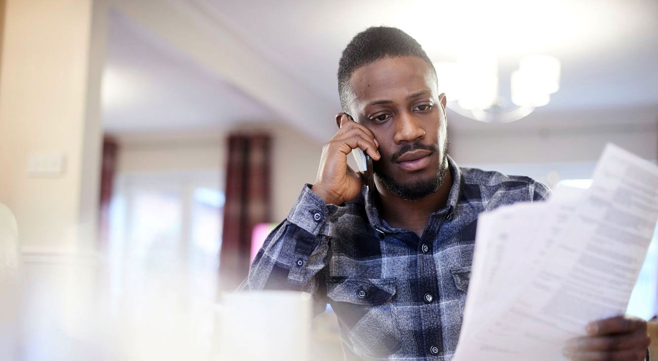 A man sitting at a table at home, reviewing documents while talking on a mobile phone.