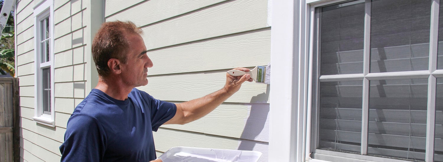 Middle-aged caucasian man painting exterior window pane of house
