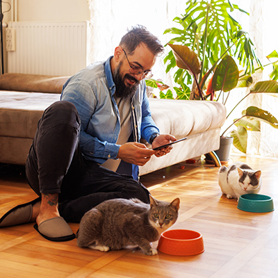 Man crouched on the floor with his cat while looking at his phone