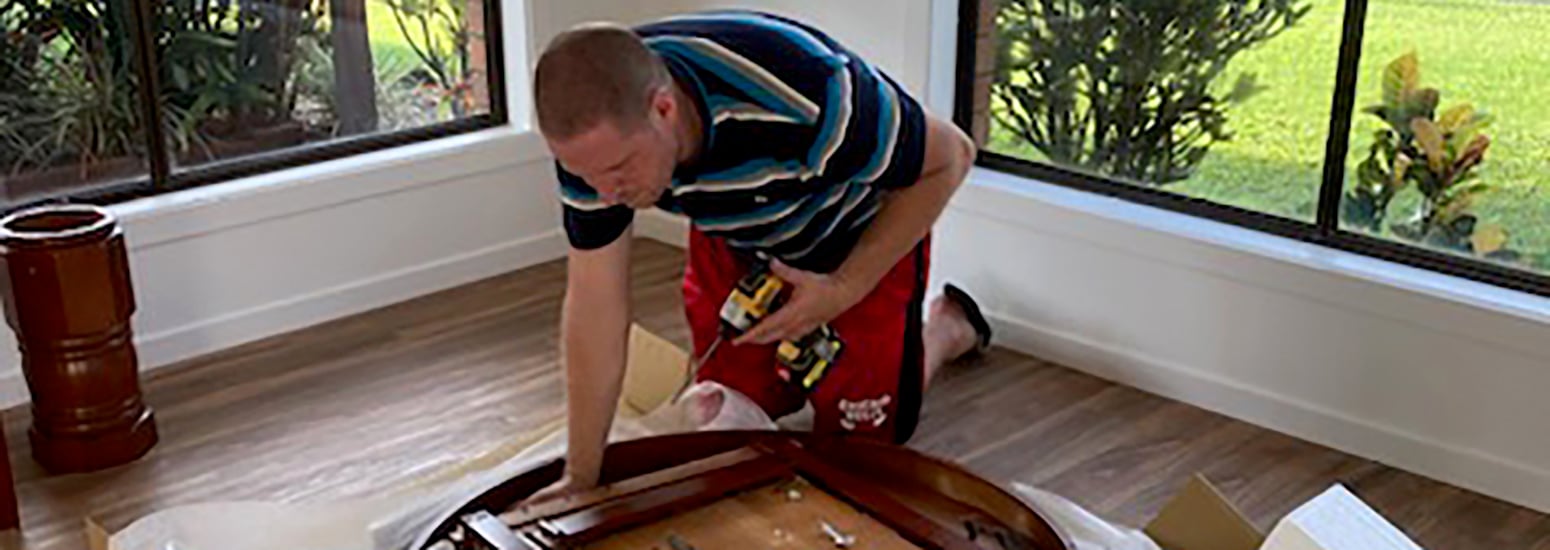 Man kneeled on floor drilling the underside of a wooden table