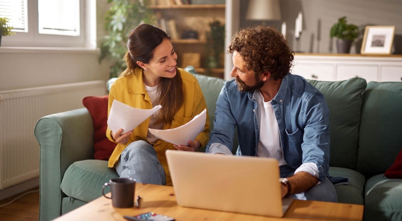 Two people reviewing household documents together at home using a laptop