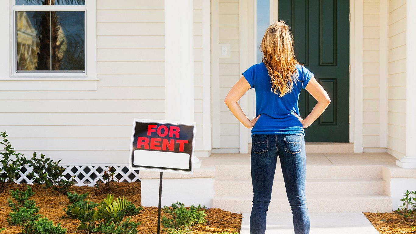 Rear view of woman standing in front of a house with a for rent sign next to her