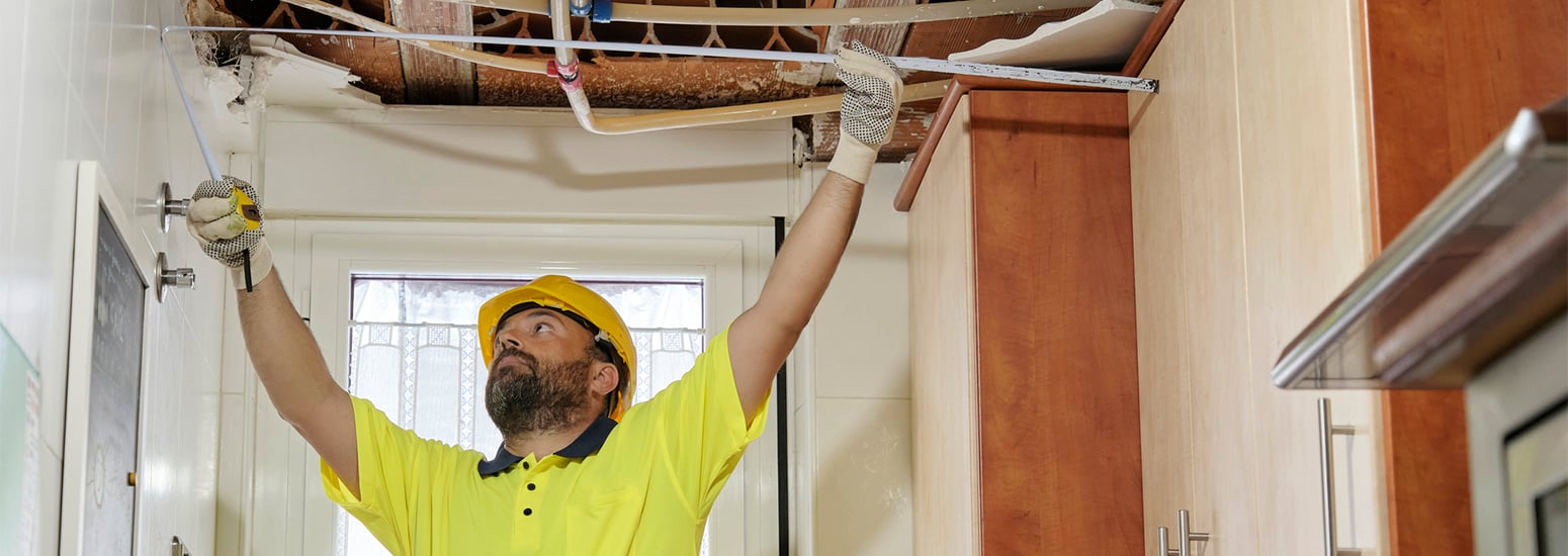 Workman using measuring tape in house wearing hard helmet and hi-vis attire