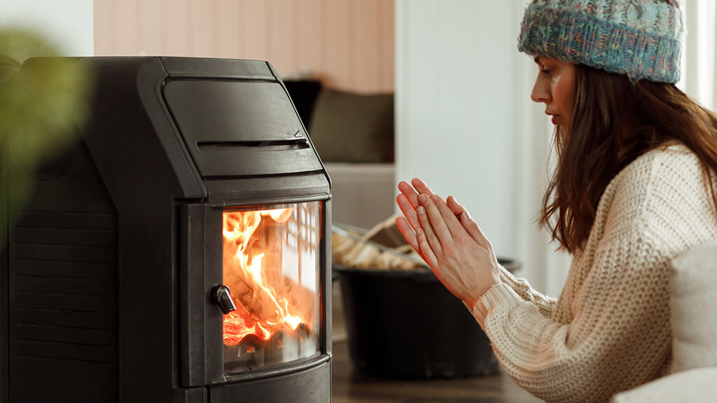 Young woman sitting at home by the fireplace and warming her hands