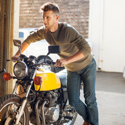 Man pushing a yellow motorbike out of a garage - to illustrate comprehensive motorcycle insurance, motorbike insurance quotes, and reliable insurance for motorcycles in Australia