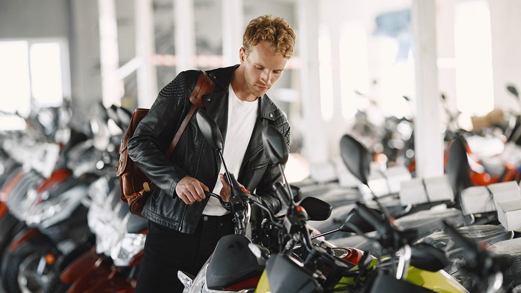 A man inspecting a motorcycle in a showroom with several bikes displayed in the background.