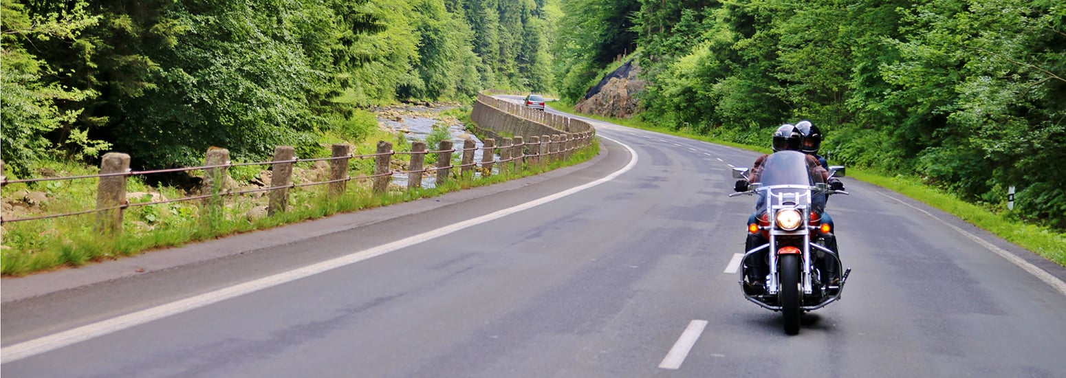 Two motorcyclists riding a cruiser bike on a winding forest road to promote motorcycle insurance or motorbike insurance that covers scenic rides in Australia.