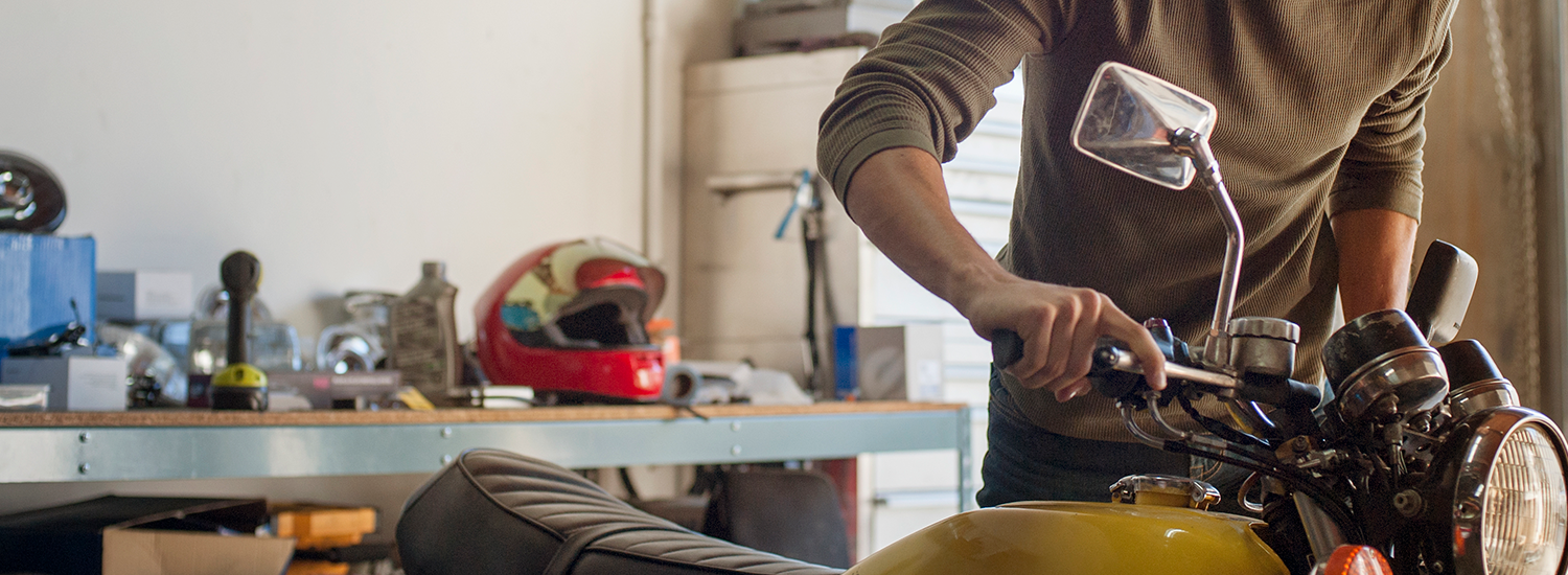 A man performing maintenance on a yellow motorbike in a garage - promoting comprehensive motorcycle insurance or motorbike insurance that covers theft, repairs, and rider protection in Australia.