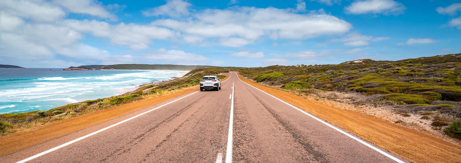 A white car driving along an Australian coastal highway, illustrating an article describing the differences between CTP insurance, Comprehensive car insurance and Third Party car insurance options for drivers.