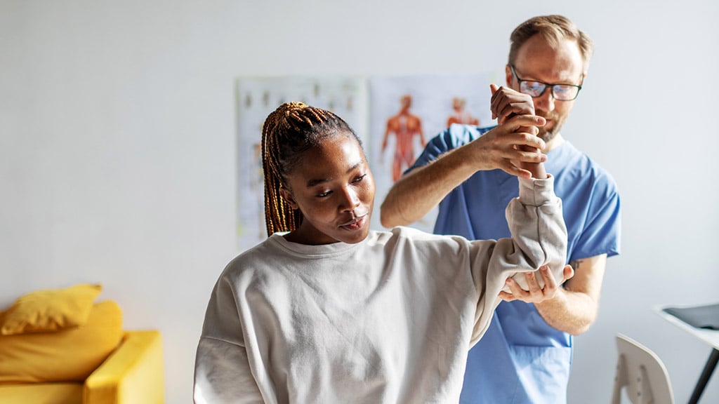 A healthcare professional supporting a worker’s arm during a clinical assessment.